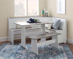 a white table with two benches in front of it and a rug on the floor