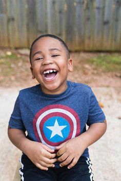 a young boy sitting on top of a wooden bench with a captain america t - shirt on