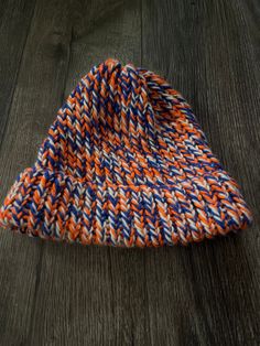 an orange and blue knitted hat laying on top of a wooden floor