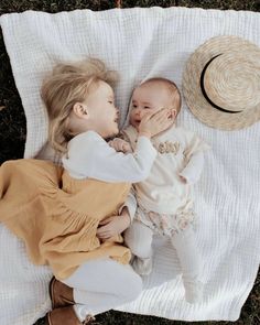 two babies laying on top of a blanket next to a hat and a straw hat