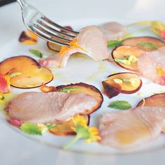 a white plate topped with slices of meat and veggies next to a fork