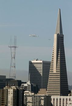 an airplane is flying in the sky over some buildings and a tower with a radio antenna