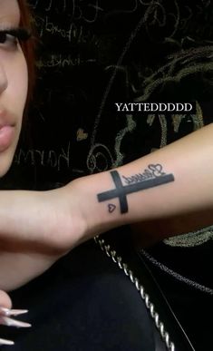 a woman with a cross tattoo on her arm and the words tattooed in black ink