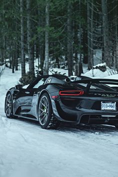 a black sports car driving down a snow covered road next to trees in the woods