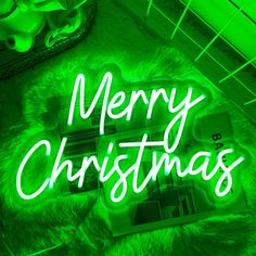 a green neon sign that says merry christmas on top of a furry surface with other items