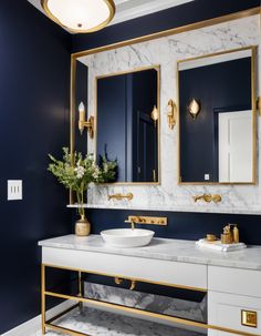 a bathroom with blue walls and gold trim, marble countertops and two white sinks