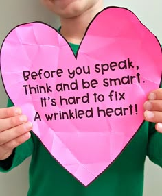 a child holding up a pink paper heart with the words before you speak, think and be smart it's hard to fix a wrinkled heart