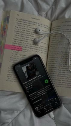 an open book with headphones on top of it next to a cell phone and earbuds