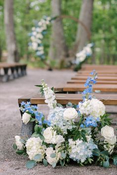 white and blue flowers are on the ground next to wooden benches with trees in the background