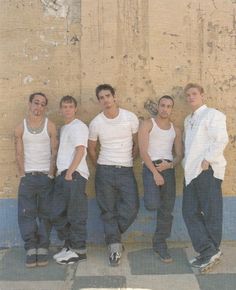 four young men standing next to each other in front of a wall with peeling paint