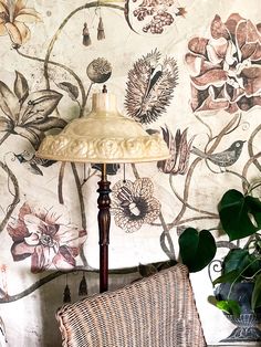 a lamp sitting on top of a wooden table next to a wall covered in flowers