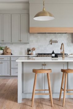 two wooden stools sit in front of an island with white countertops and gray cabinets