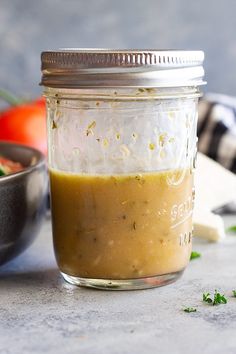 a glass jar filled with dressing next to a bowl of vegetables and other food items