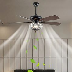 a living room with a black couch and green leaves on the ceiling fan that is lit up