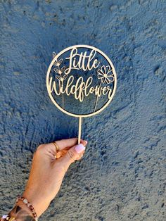 a person holding up a wooden sign that says little wildflower