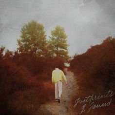 a person walking down a dirt road in the woods with trees on either side and an overcast sky above