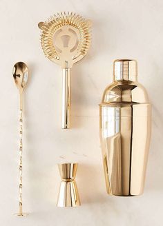 a set of three gold cocktail shakers and spoons on a white counter top