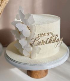 a white birthday cake with flowers on top and happy birthday written on the side in gold lettering