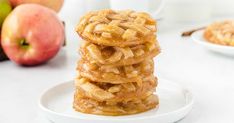 a stack of apple pie cookies sitting on top of a white plate next to apples