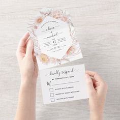 two hands holding up a white wedding card with flowers on the front and back side