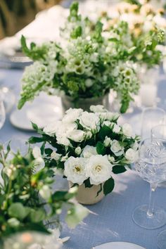 the table is set with white flowers and greenery in vases on each side