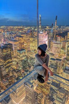 a woman standing on the edge of a high rise in front of city lights at night