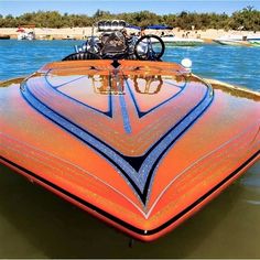 an orange and blue boat in the water with other boats on the shore behind it