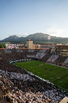 a football stadium filled with lots of people watching the game in front of some mountains