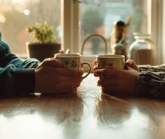 two people sitting at a table holding coffee mugs with their hands on each other