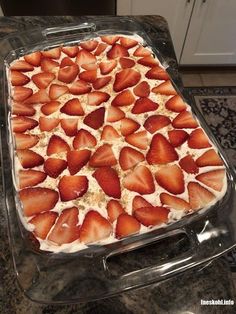 a cake with strawberries on it in a glass dish sitting on top of a counter