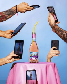 several people holding their cell phones in front of a table with a bottle of wine on it