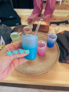 a hand holding a blue cup with two different colored cups in it and some other items on the table