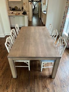 a dining room table with white chairs in the center and an open kitchen area behind it