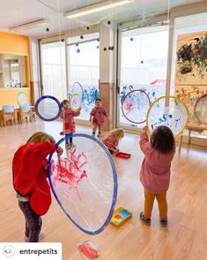 three children are playing with plastic discs in a room filled with wooden floors and large windows