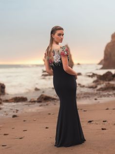 a woman standing on top of a beach next to the ocean wearing a black dress