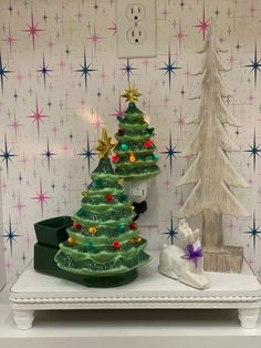 two small christmas trees are sitting on a table in front of a wallpapered background