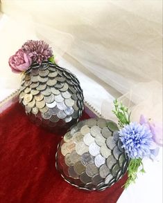 two vases filled with coins and flowers sitting on a red cloth covered tablecloth