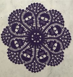 a purple doily on a white surface with holes in the middle that are crocheted