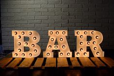 the word bar is lit up in front of a brick wall and wooden pallets