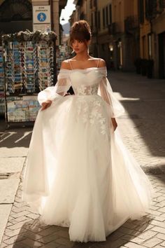 a woman is walking down the street wearing a white dress with sleeves and flowers on it