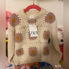 a white sweater with pink and yellow flowers hanging on a rack next to stuffed animals