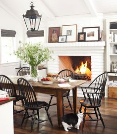 a dining room table with chairs and a fire place in the fireplace, next to a black and white cat