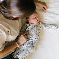 a woman laying on top of a bed next to a baby in a white shirt