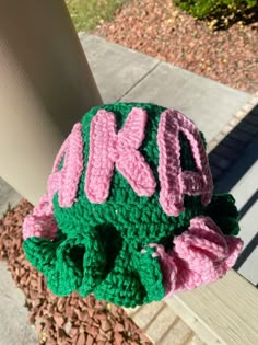 a green and pink crocheted hat with the word kkd on it