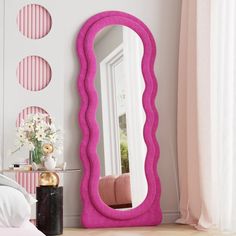 a pink mirror sitting on top of a table next to a white bed in a room