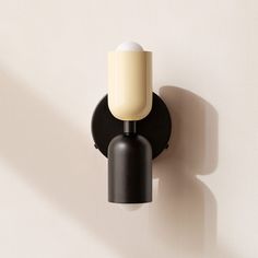 a black and white light fixture on a wall with a shadow from the left hand side