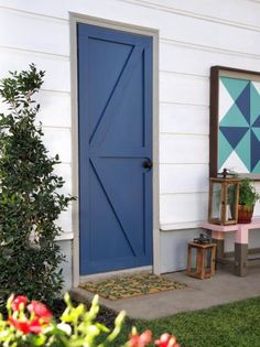 a blue door sits in front of a white house with potted plants next to it