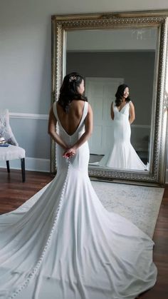 a woman standing in front of a mirror wearing a wedding dress