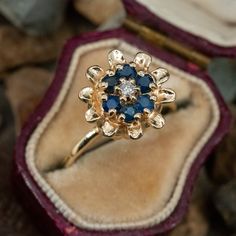 a gold ring with blue and white stones in it's velvet presentation box on rocks