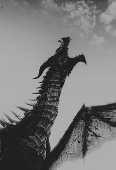 a black and white photo of a dragon flying in the sky with its wings spread